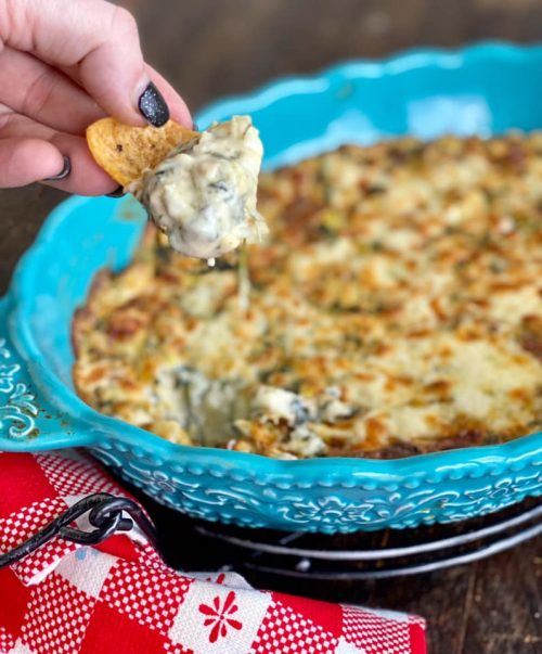 Spinach artichoke alfredo dip being scooped onto a chip