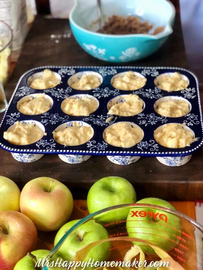 Apple pie muffins in a baker with a batter bowl and fresh apples