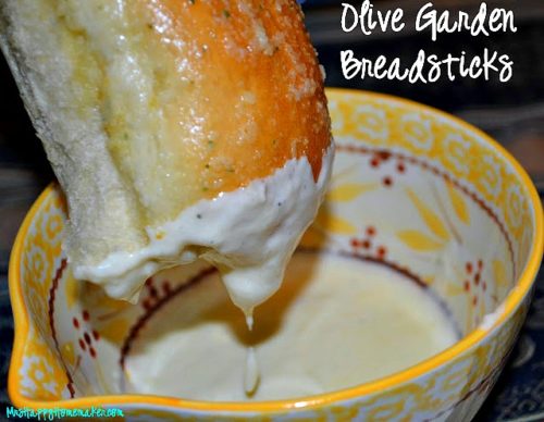 Copycat Olive Garden Breadsticks being dipped into Alfredo sauce in a yellow bowl