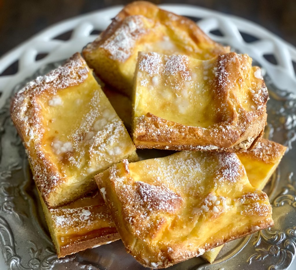 Closeup of Gooey butter cake, sliced into squares On a white plate