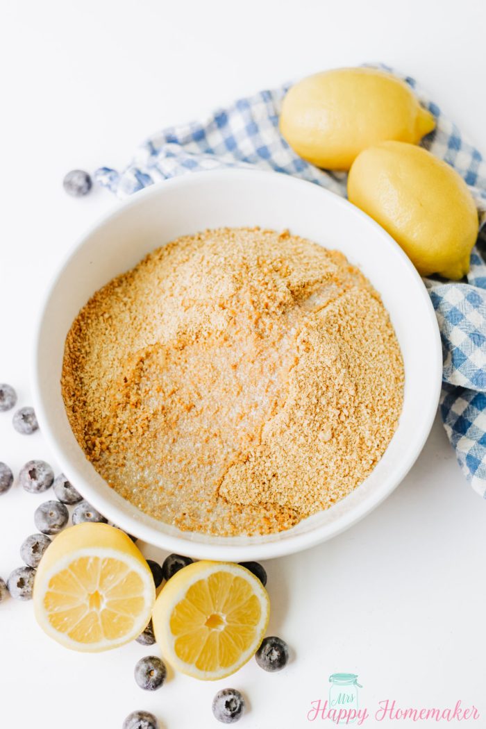 graham cracker crumbs with melted butter in a white bowl surrounded by cut up lemons