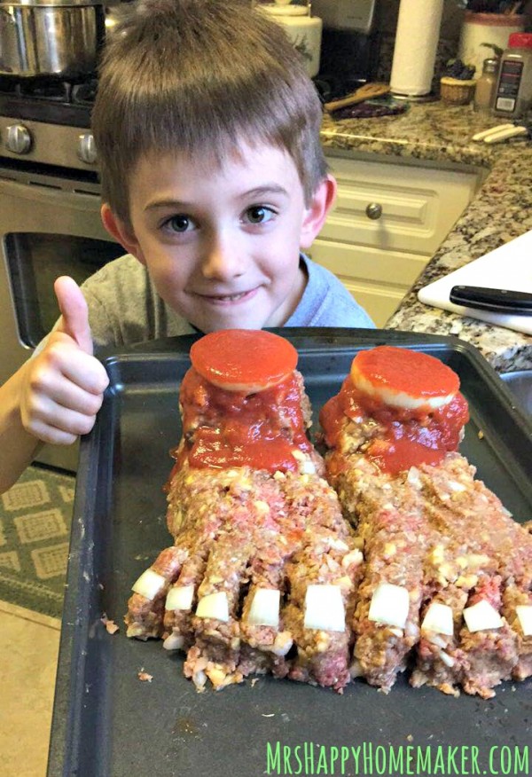 Little boy giving a thumbs up beside Halloween Feetloaf - as in a delicious meatloaf crafted to look like a pair of feet. Perfect creepy dinner for Halloween! | MrsHappyHomemaker.com @thathousewife