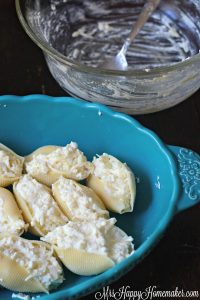 Cheese Lover's Stuffed Shells unbaked in a blue dish with an empty glass bowl