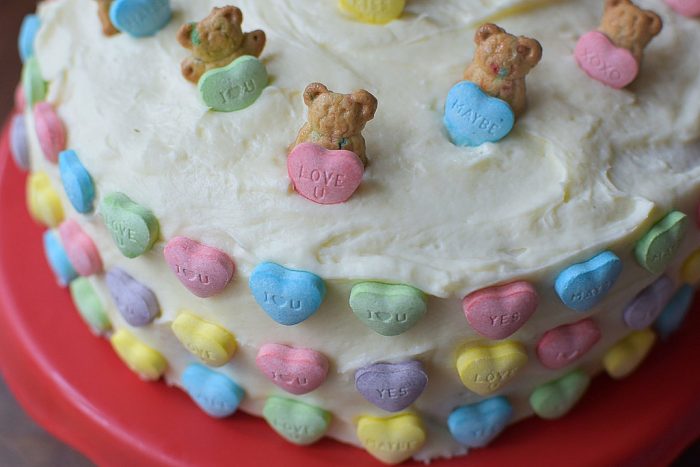 Easy Teddy Graham Valentine's Cake on a red cake stand with conversation hearts all over the cake
