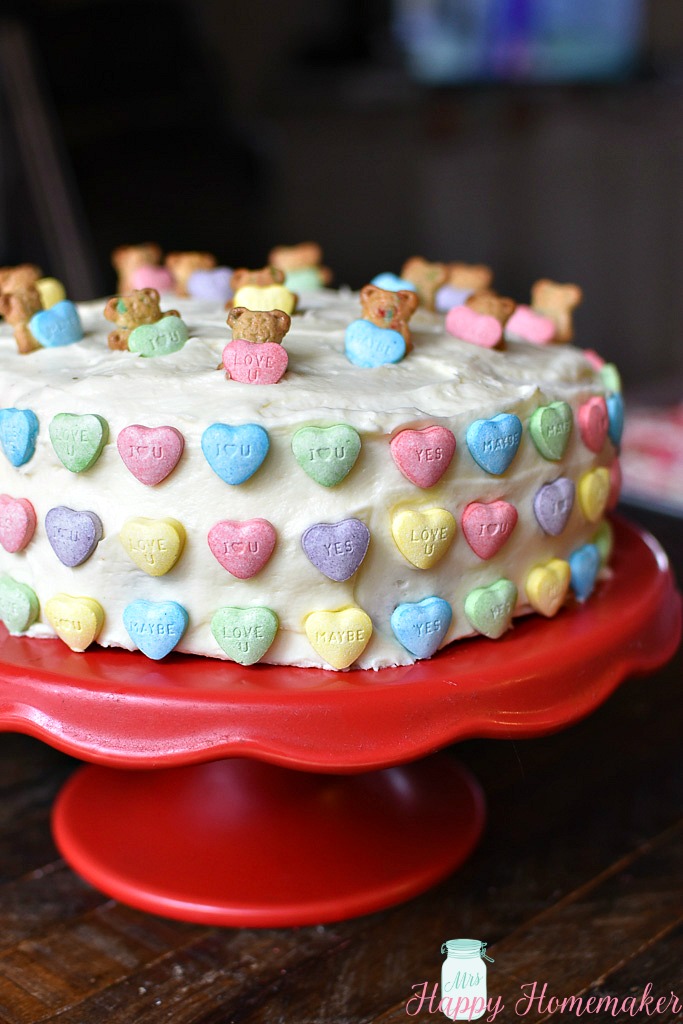 Easy Teddy Graham Valentine's Cake on a red cake stand with conversation hearts all over the cake