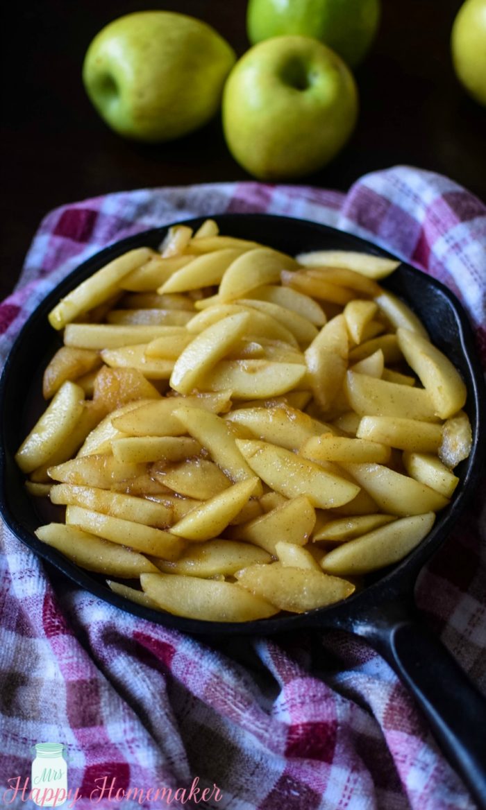 Skillet Apples in a cast iron skillet on a gingham napkin surrounded by green apples 