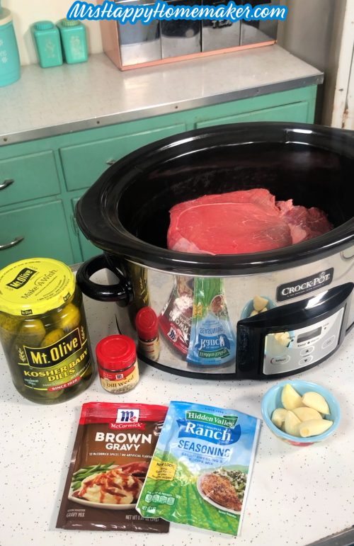 Dill Pickle Pot Roast ingredients - pickles, chuck roast in the crockpot already, jar of pickles, brown gravy packet, ranch packet, garlic, dill weed