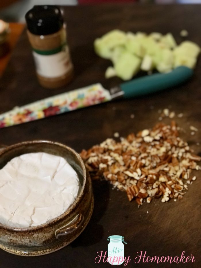 Brie, chopped pecans, chopped apples, and a container of ground cinnamon on a cutting board