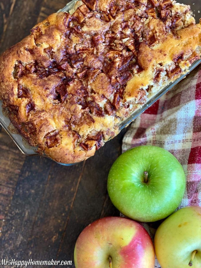 Apple fritter bread in a loaf pan with fresh apples around it