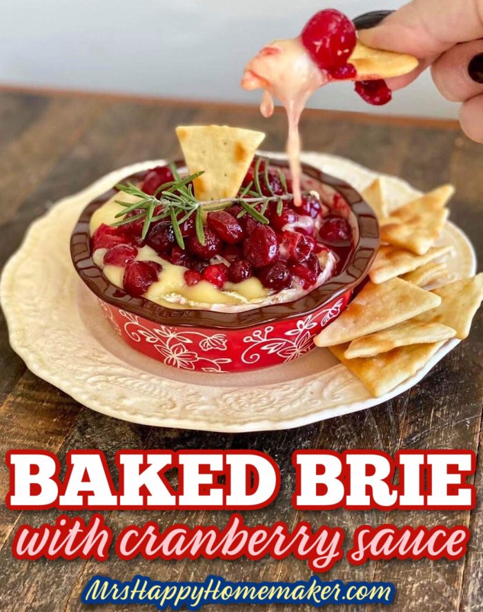 Baked Brie with Cranberry Sauce on top - a hand is using a pita chip to dip inside it 
