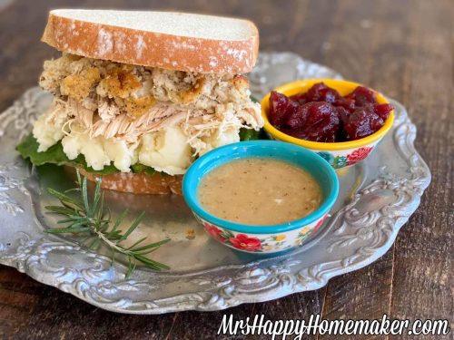 Thanksgiving sandwich - sandwich with turkey, dressing, mashed potatoes on a silver plate with a bowl of gravy and a bowl of cranberry sauce