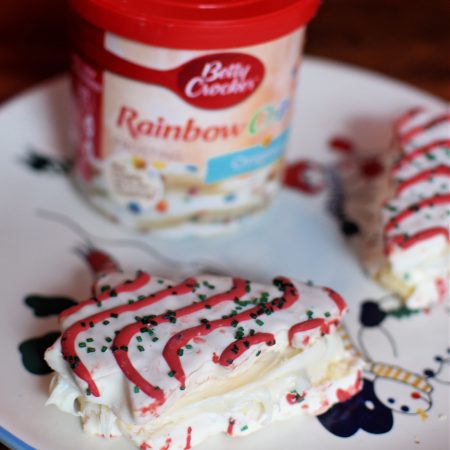 a container of frosting on a snowman plate with little debbie Christmas tree cakes