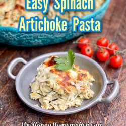 Spinach alfredo pasta in a round silver handled dish with cherry tomatoes beside it
