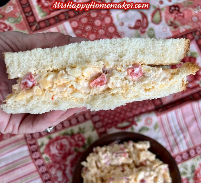 the Masters’ pimento cheese - some in a brown bowl and some spread inside of a sandwich being held by a hand