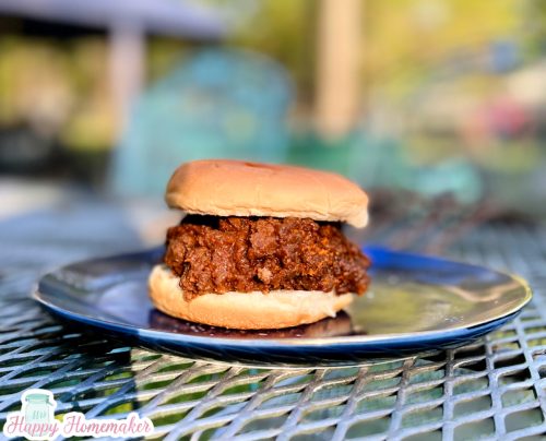 Homemade sloppy joes on a burger bun on a blue plate On an outside wire table