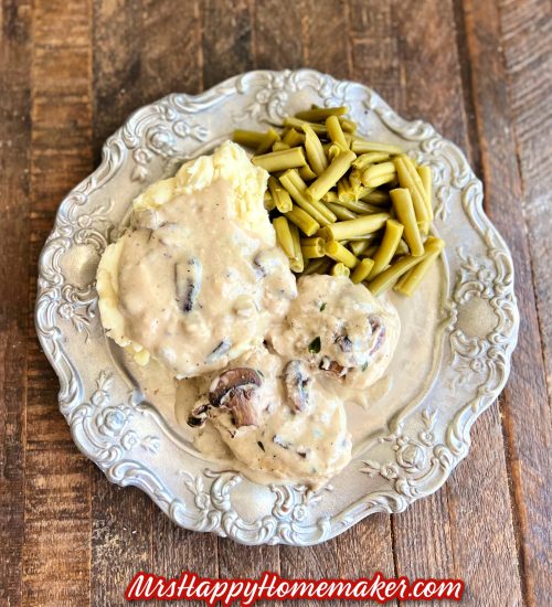 Mushroom pork chops with gravy on a pewter plate with mashed potatoes and green beans