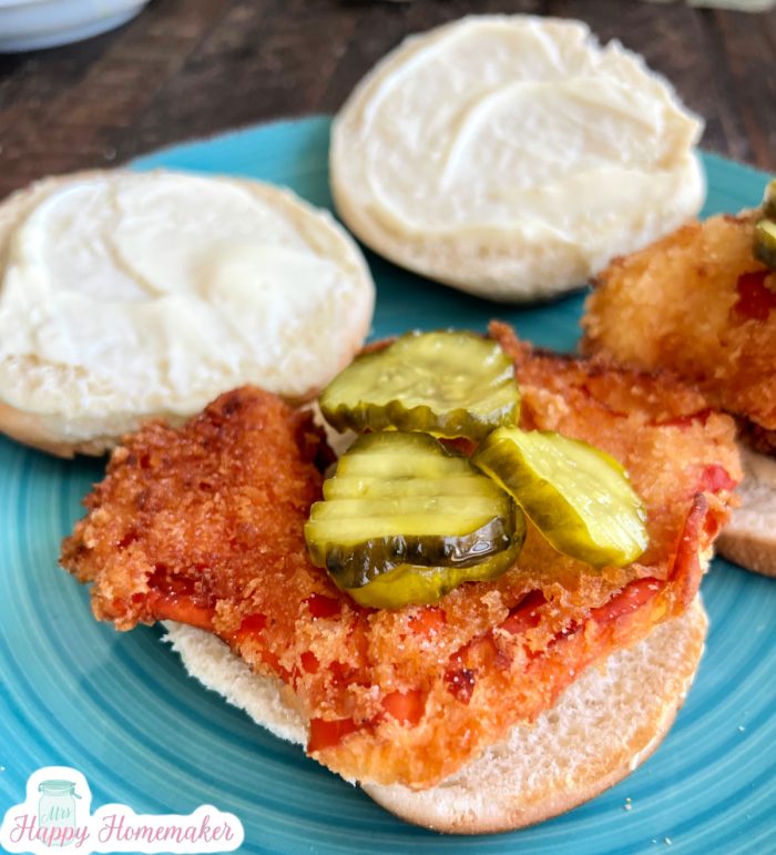 Vegetarian chick-fil-a chicken sandwich on a blue plate, topped with pickles and the top bun laying on the side of the bottom half of the sandwich