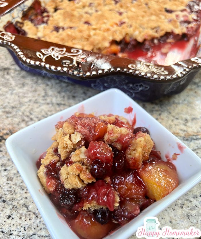 Peach Blueberry Crisp in a 9x13 brown and blue casserole dish With a serving in a small white dish