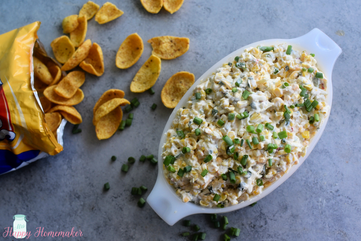 Creamy Mexican corn dip in a vintage Pyrex dish with corn chips laying on the table beside of it 