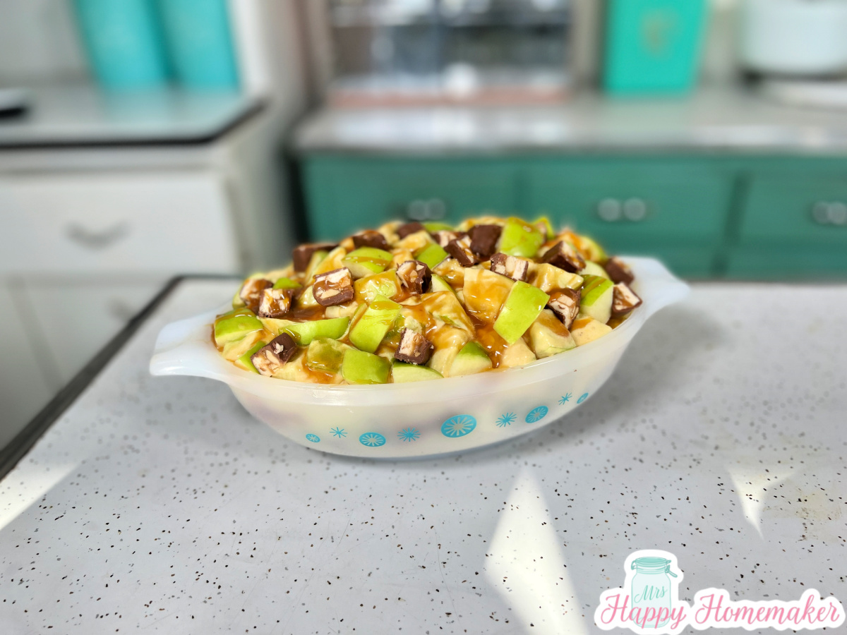 Snickers apple salad in a casserole dish in a vintage 50’s kitchen background