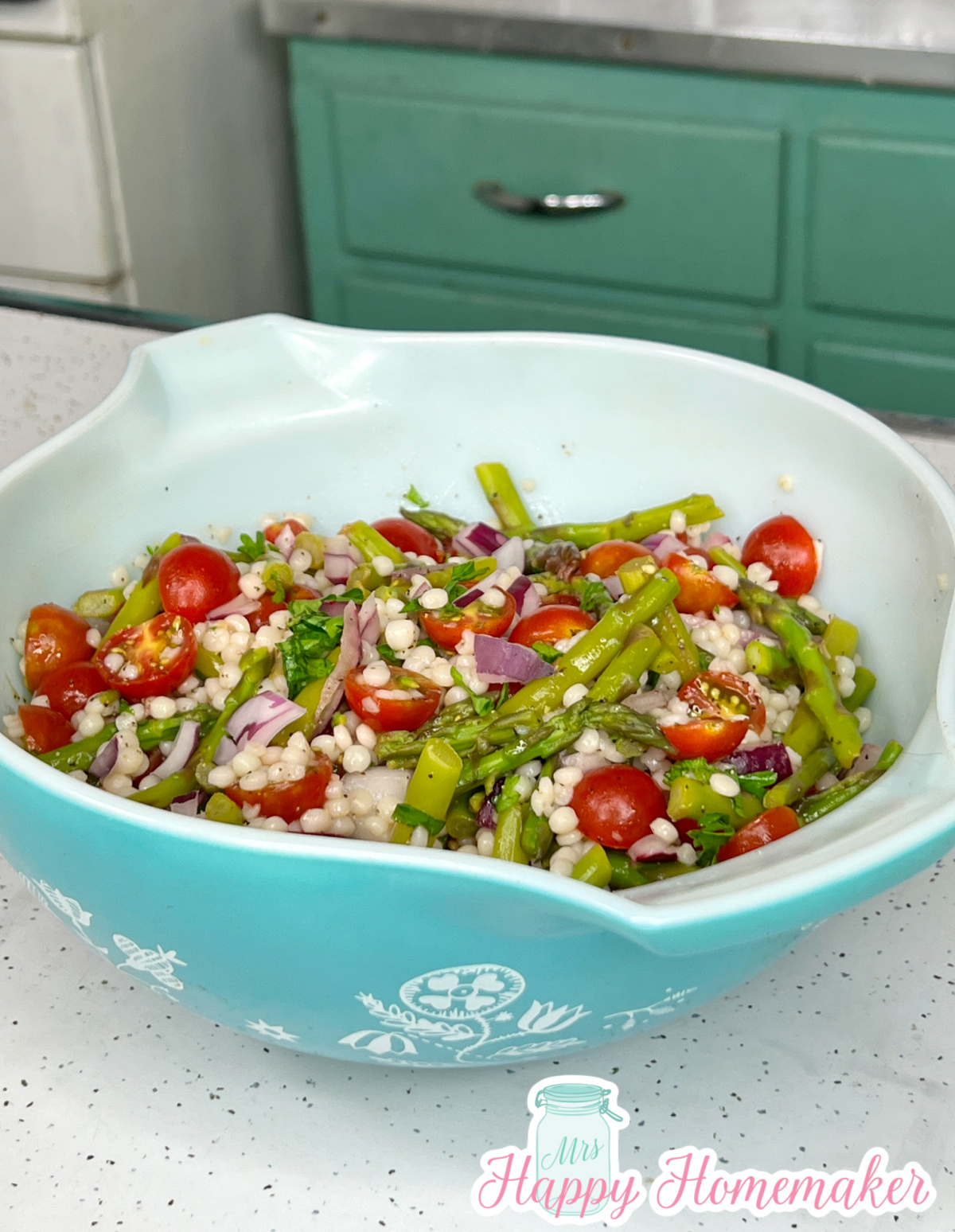 Closeup of pearl couscous salad with asparagus & cherry tomatoes in a vintage blue Pyrex bowl