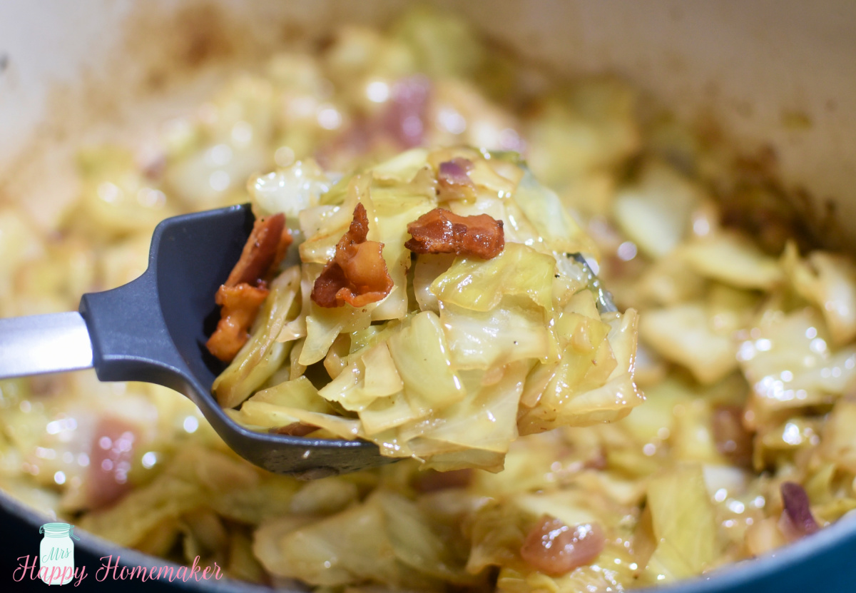 Braised cabbage being scooped from a blue pot with bacon