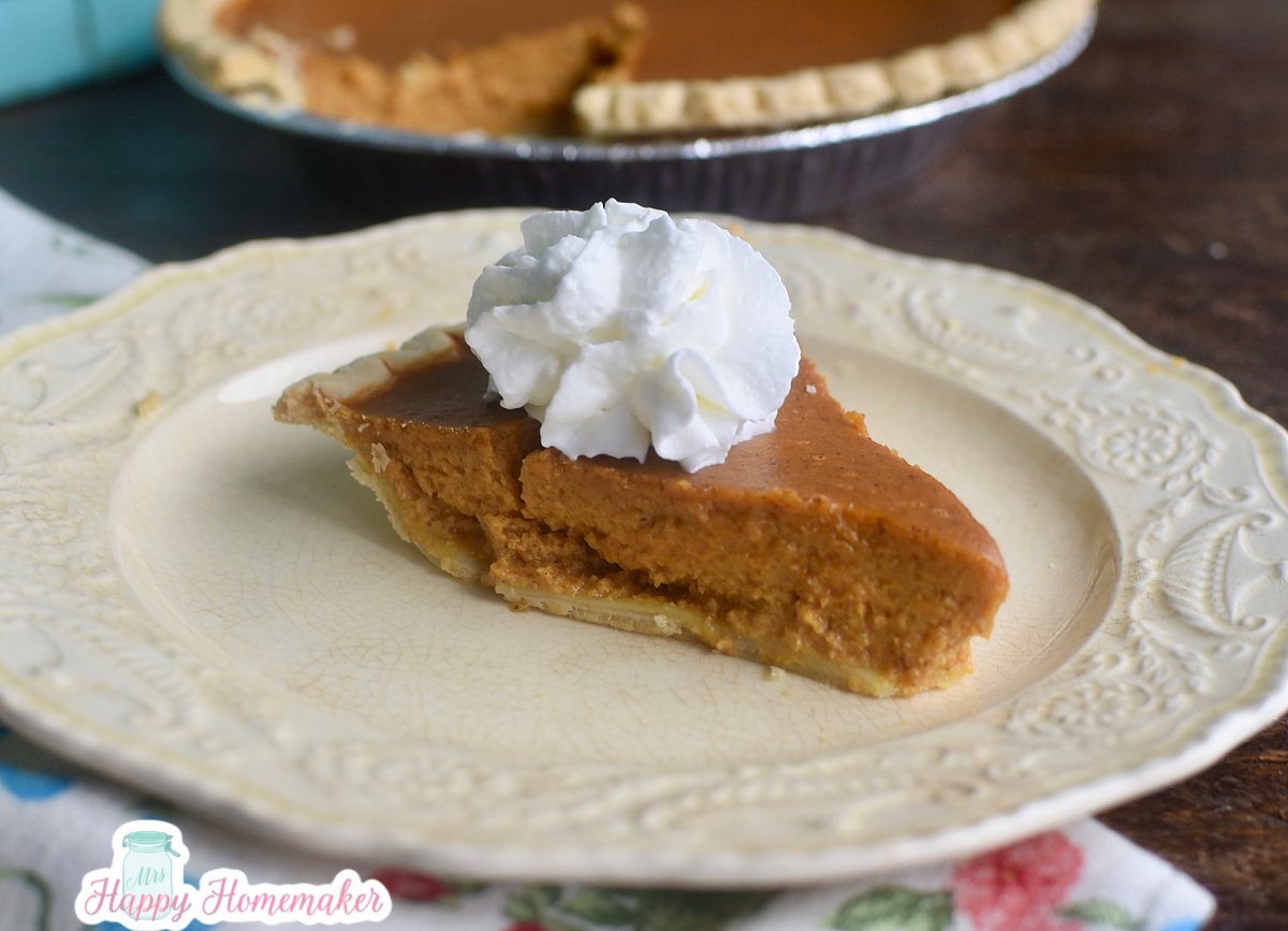 A pumpkin pie slice with whipped cream on a white plate