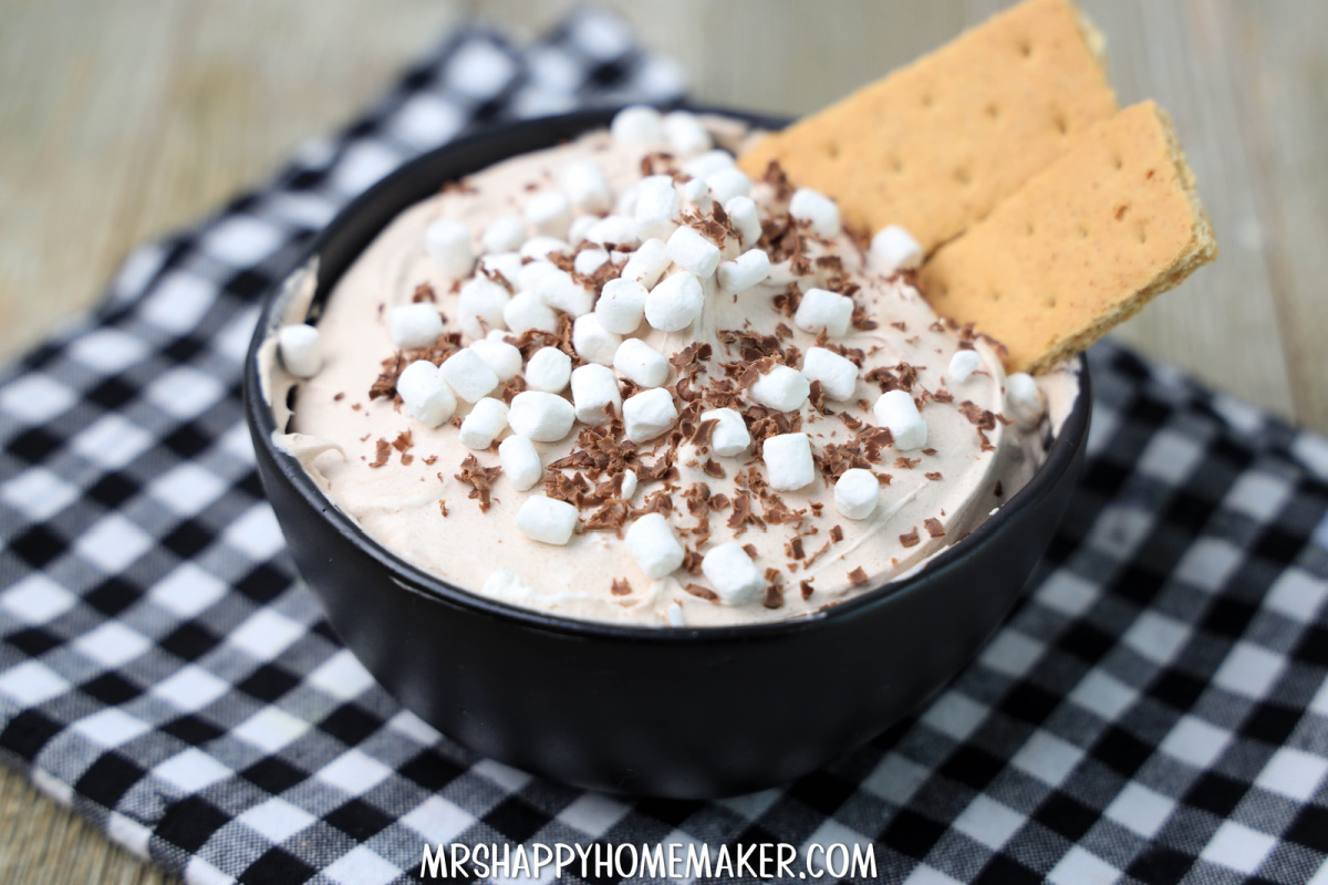 Hot chocolate dip with mini marshmallows and graham crackers on top on a Buffalo plaid cloth