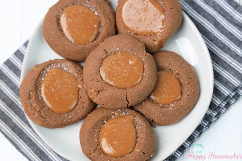 Salted caramel thumbprint cookies on a white plate sitting a striped napkin
