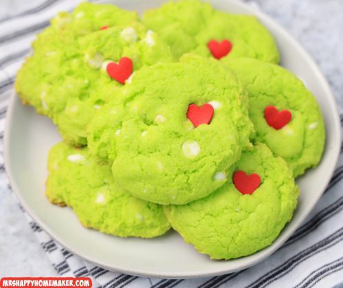 A white plate filled with green grinch cookies with a red heart in them