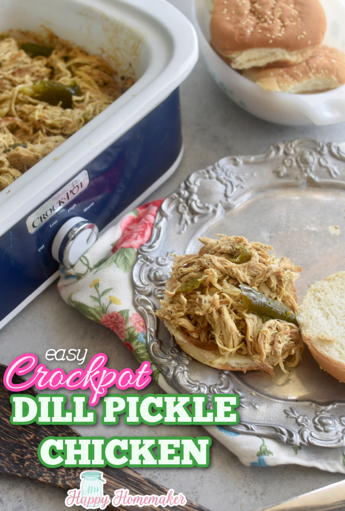 Dill Pickle chicken in a crockpot and piled on a bun thats on a plate beside the crockpot