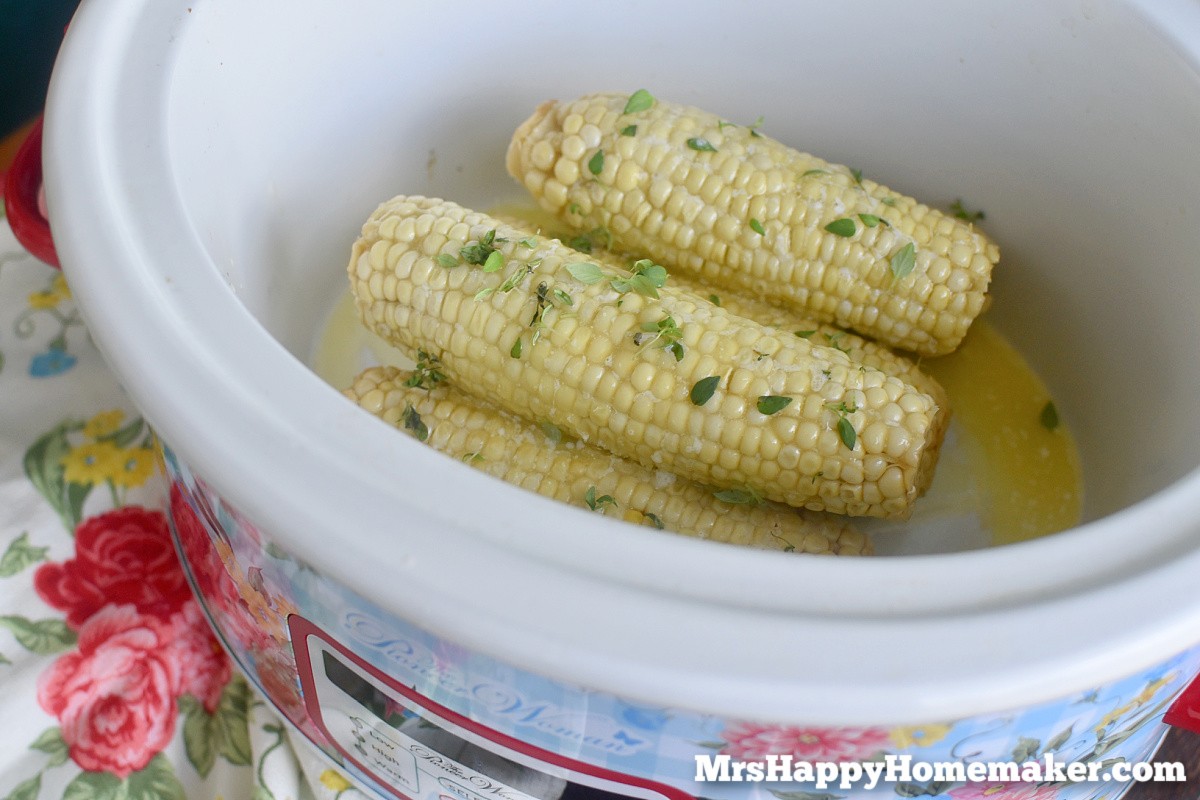 Corn on the cob in a white crockpot sprinkled with fresh herbs