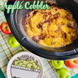 Apple cobbler in a black crockpot with an ‘apple pie’ design plate beside of it
