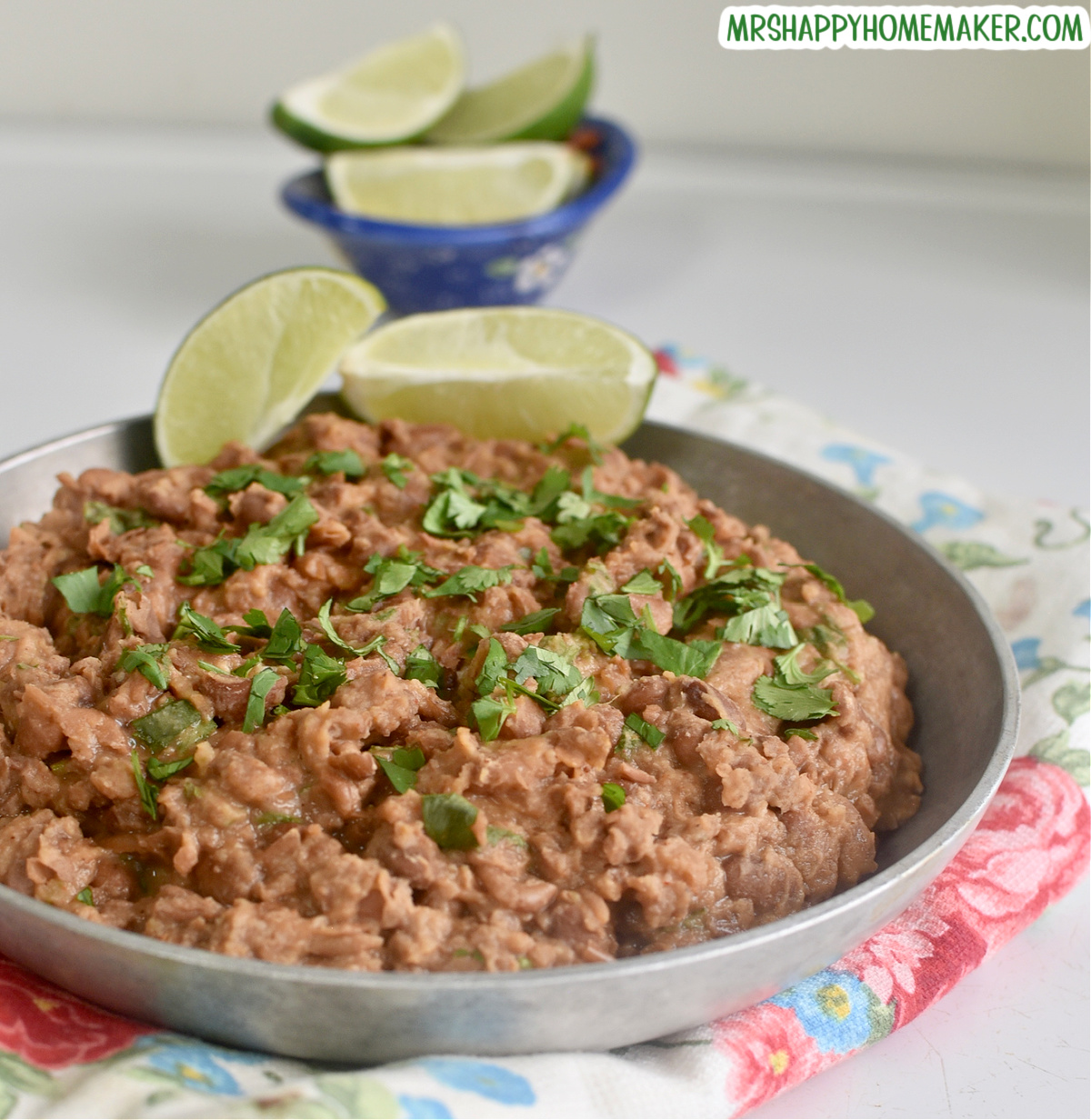 Easy homemade refried beans in a round silver bowl beside a small blue bowl of lime slices