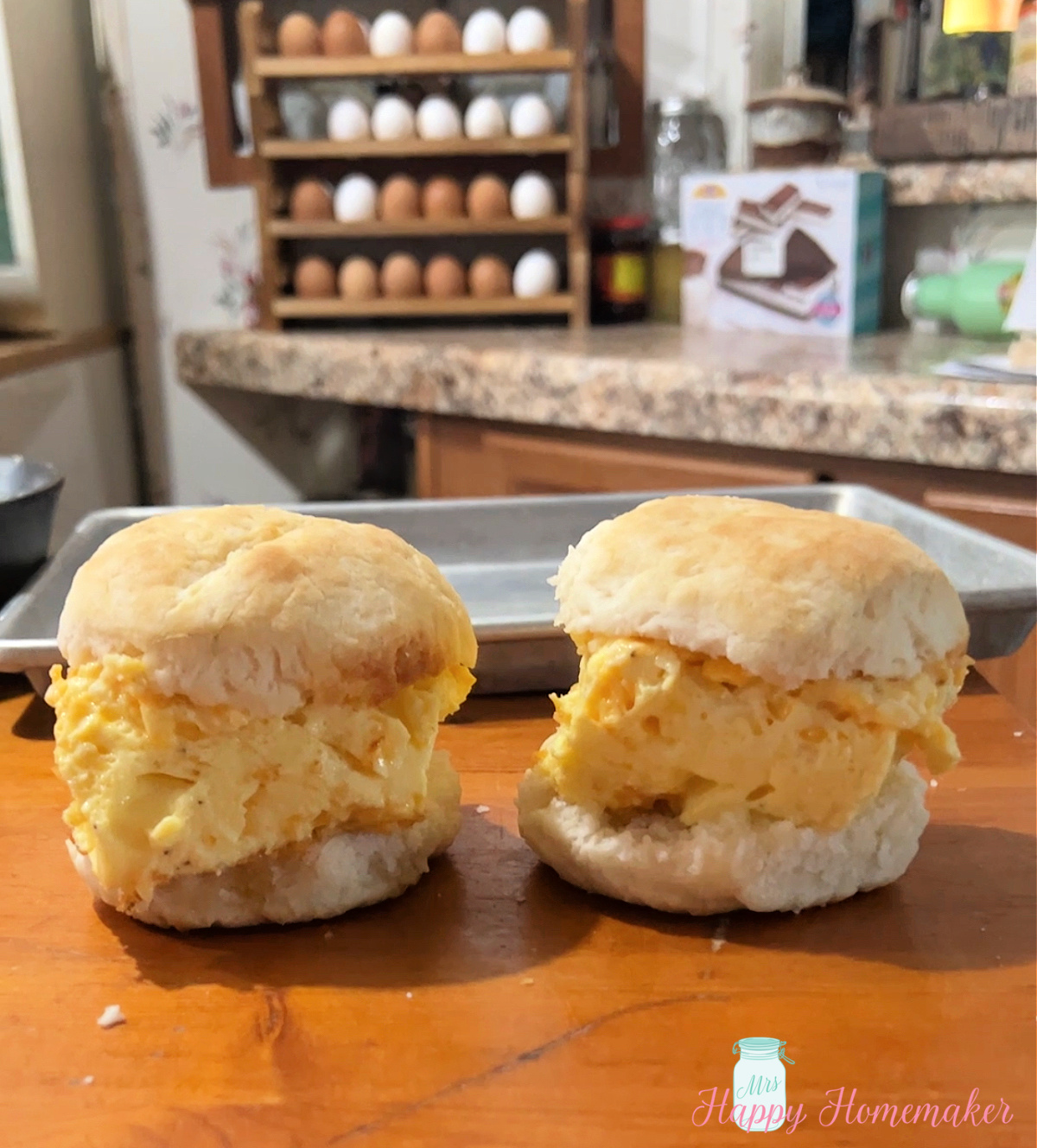 Two baked egg breakfast biscuit sandwiches sitting on a wooden counter 