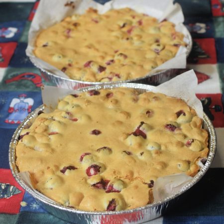 Cranberry Christmas Cake in two round aluminum pans that are lined with parchment paper, set on a holiday tablecloth