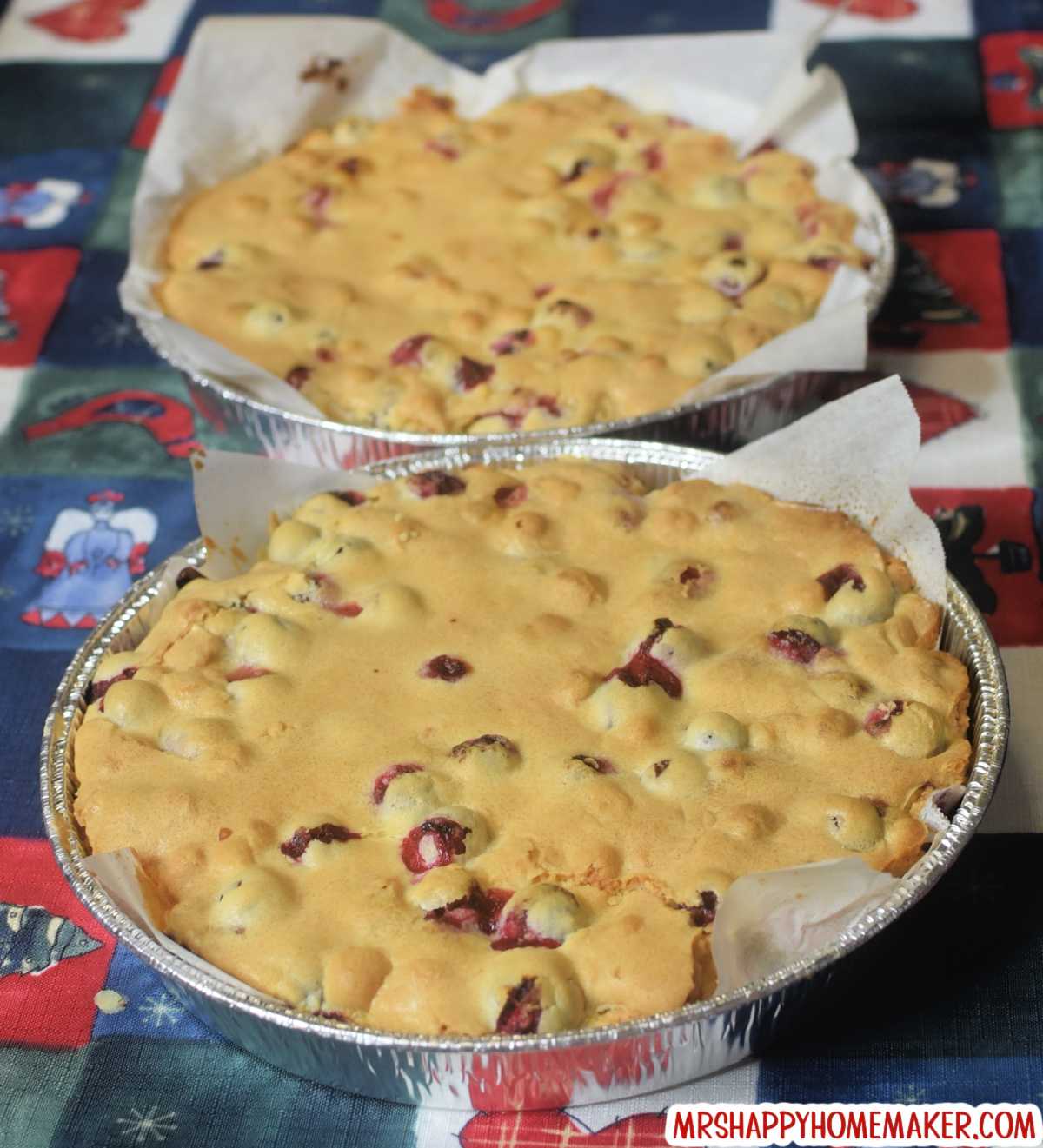 Cranberry Christmas Cake in two round aluminum pans that are lined with parchment paper, set on a holiday tablecloth 