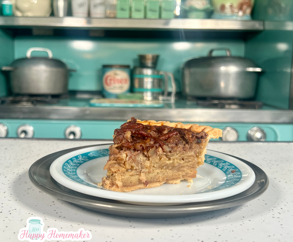 Apple pecan pie slice on a blue rimmed white plate - with a vintage blue stove behind it