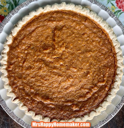 Sweet potato pie on a white pie dish with a floral towel beside of it