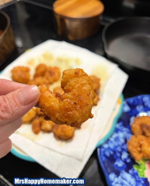 Southern fried shrimp being held in a hand over a stove