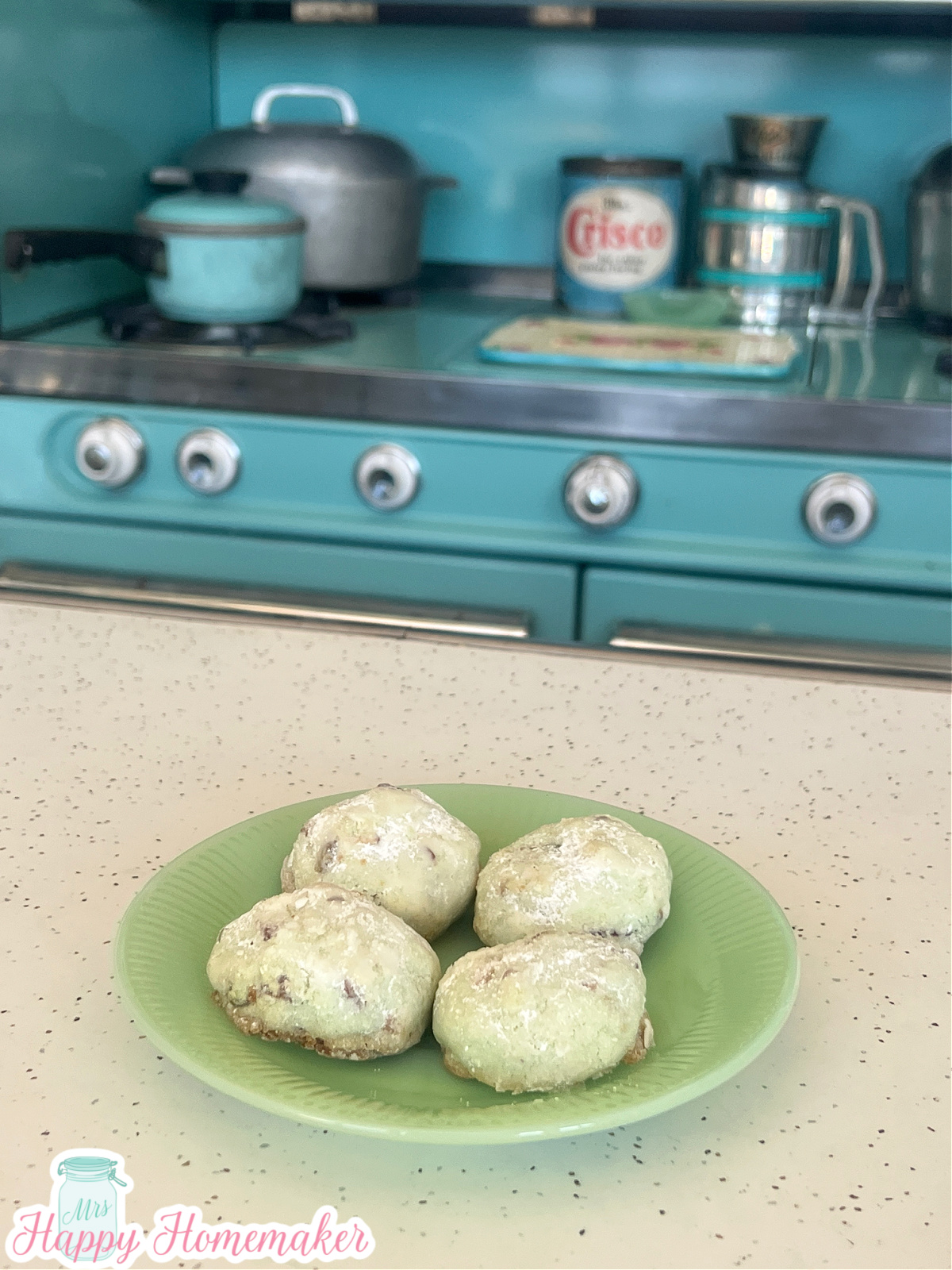 Pistachio Wedding Cookies on a jadeite plate on a white countertop infront of a vintage blue stove