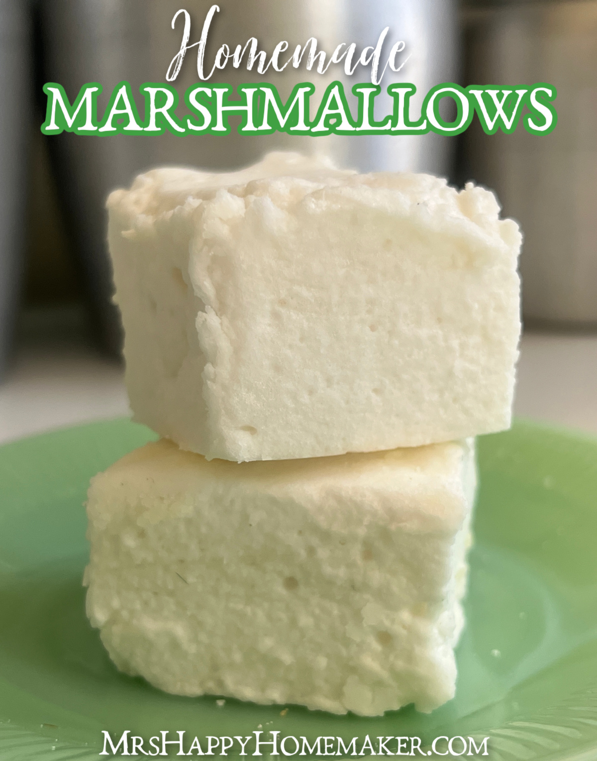 Two homemade marshmallows stacked on top of each other sitting on a green jadeite plate with a silver canister behind them