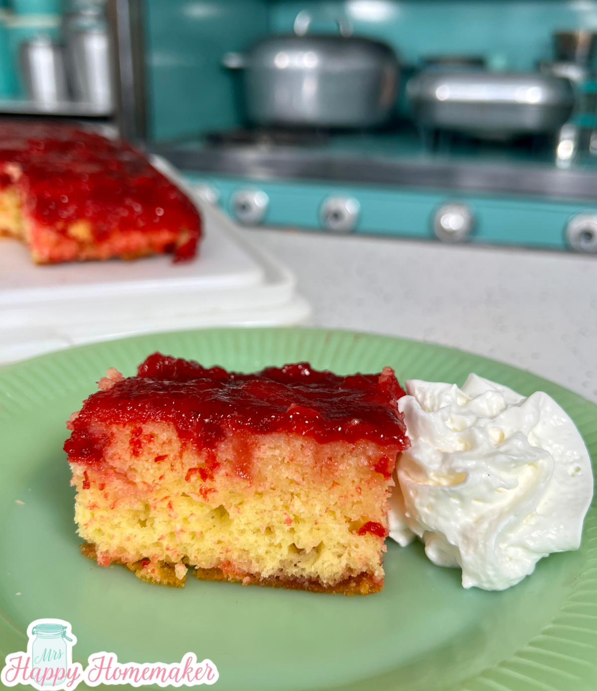Strawberry Upside Down Cake on a green plate with a dollop of whipped cream on the side. There is a blue stove in the background
