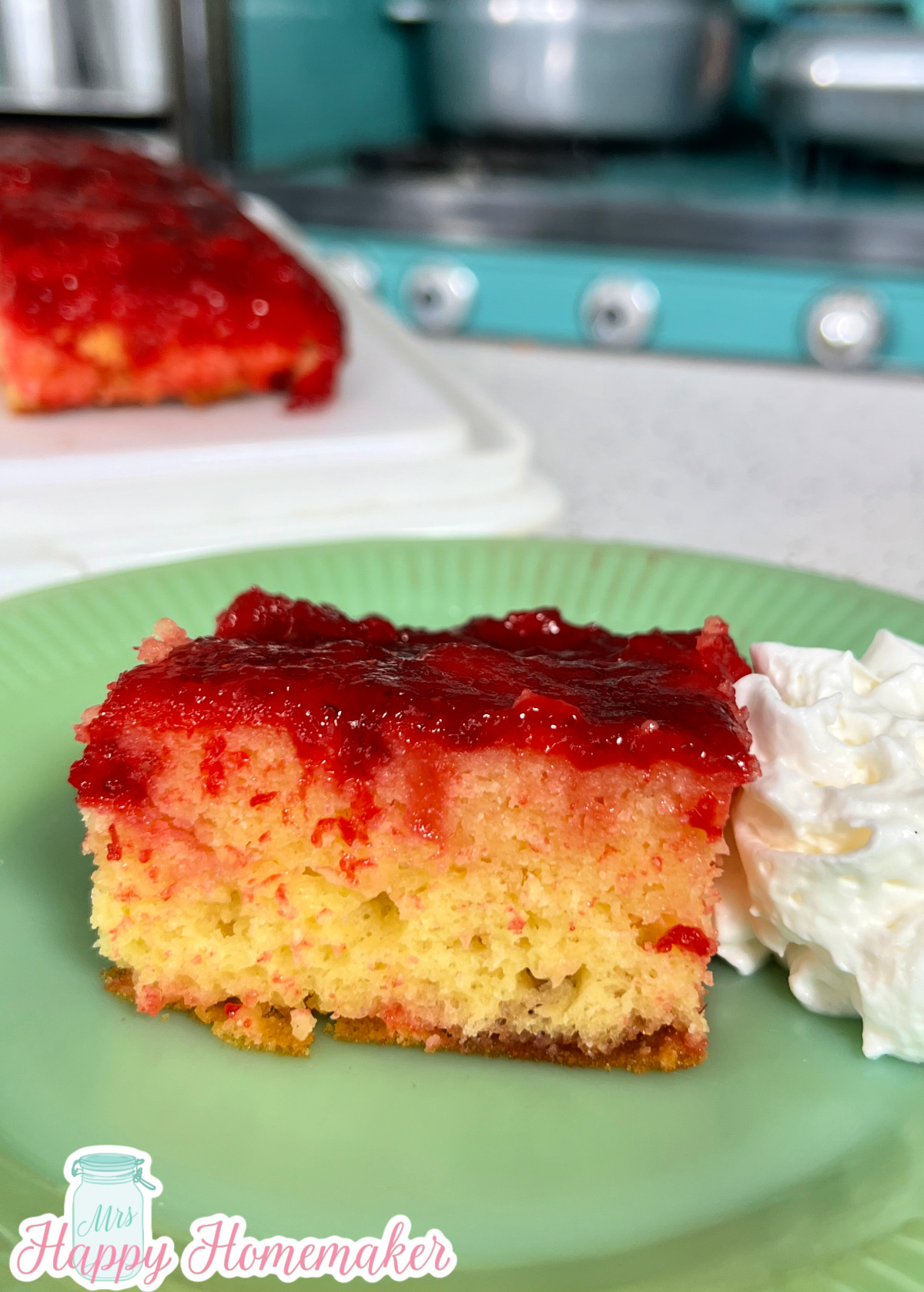 A slice of strawberry upside down cake on a green plate with a blue stove in the background