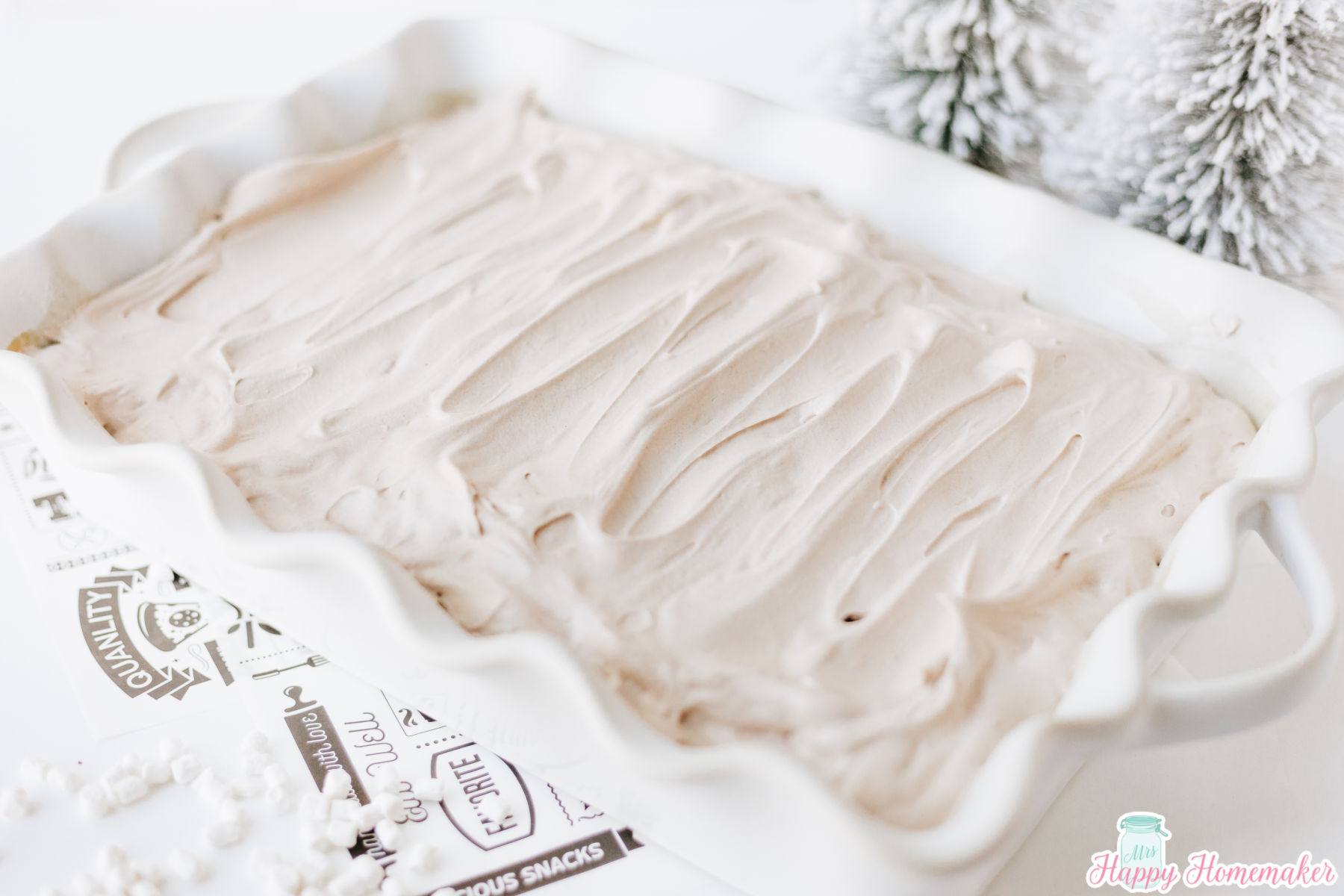 frosted hot cocoa poke cake in a rectangle white cake dish on a white background