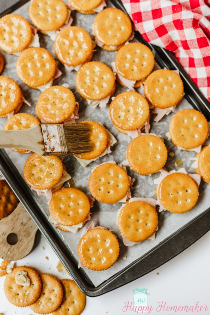 Ritz Cracker Party Sandwiches on a baking sheet with butter sauce being brushed on with a pastry brush