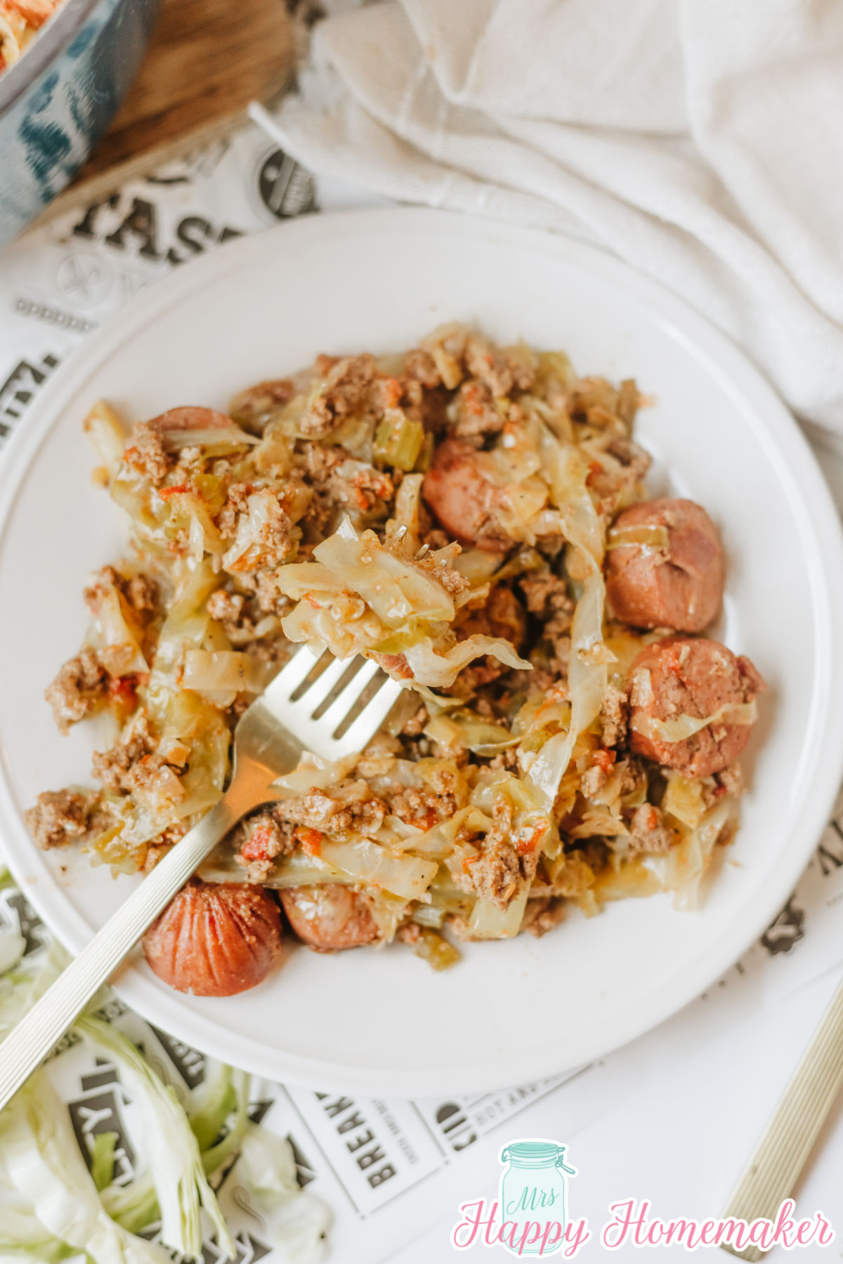 dirty cabbage on a white plate with a fork holding up a piece of smoked sausage