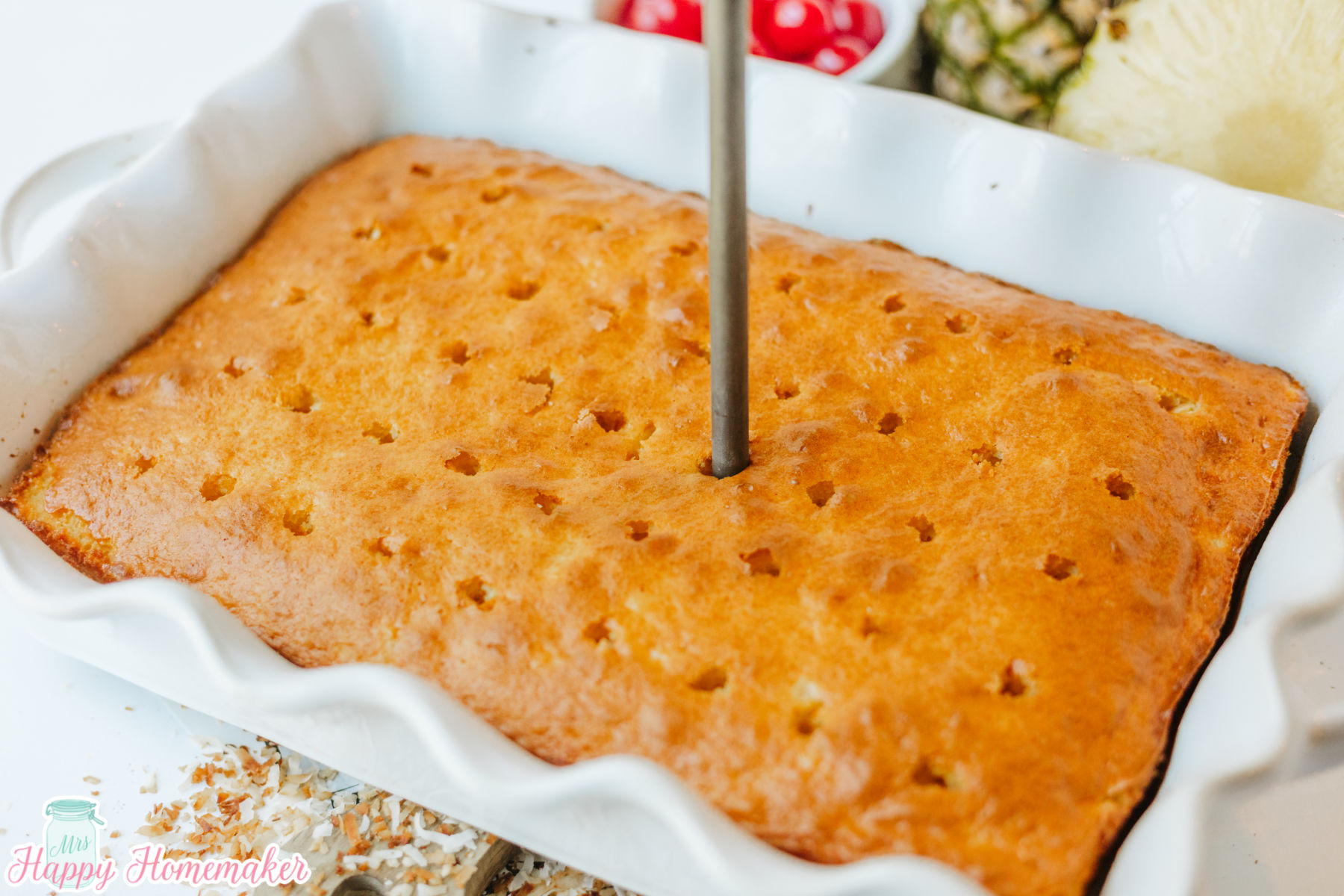 Simple & Easy Pina Colada Poke Cake with holes being poked in it with the end of a wooden spoon