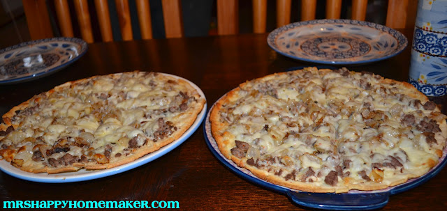 Philly cheesesteak pizza - 2 of them on a tabletop with plates behind them for serving 