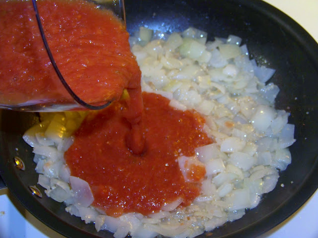 Pouring tomato sauce into the sautéed onions and garlic in a skillet
